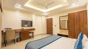 Habitación de hotel con cama, escritorio, silla, televisor, armario y ventilador de techo.