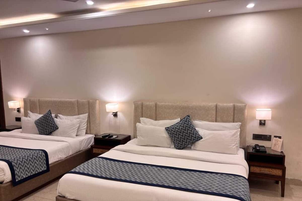 A hotel room with two beds, each with a headboard, bedside tables, and lamps.