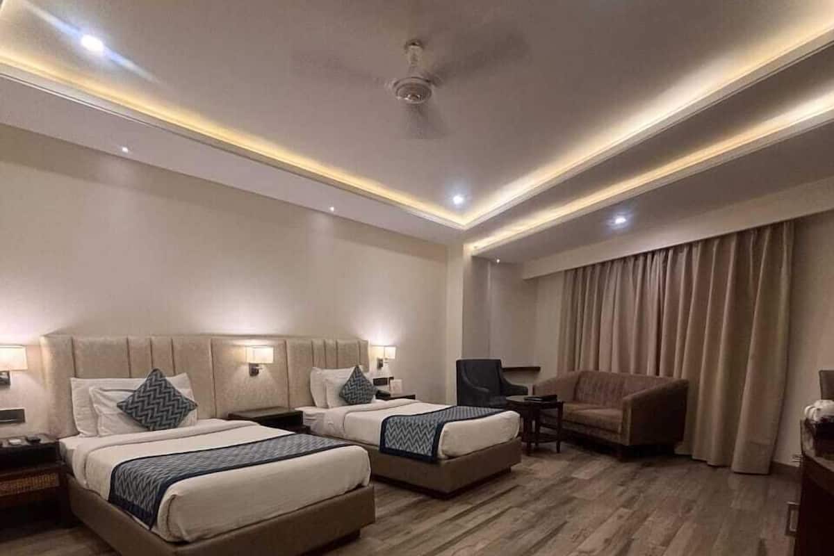 A hotel room with two beds, a sofa, a TV, and a ceiling fan.