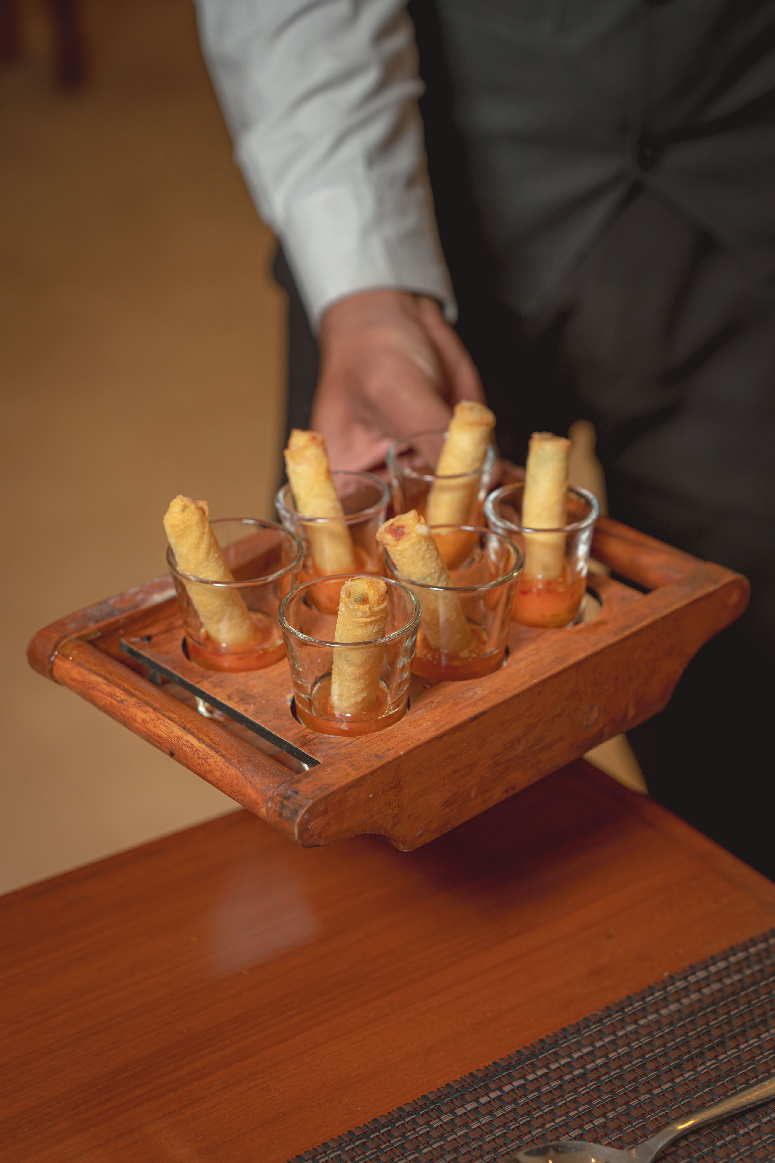 A tray with several glasses containing a food item, likely appetizers, being held by a person.
