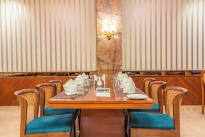A hotel dining room with a marble column, a long table set for a meal, and cushioned chairs. - MJ AERO SUITE (Rishikesh)
