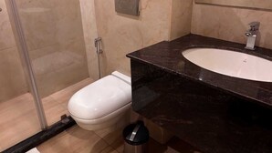 A bathroom with a white toilet, a sink with a dark countertop, and a shower area. - MJ AERO SUITE (Rishikesh)