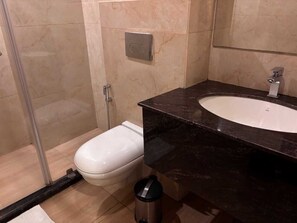 A bathroom with a white toilet, a sink with a dark countertop, and a shower area. - MJ AERO SUITE (Rishikesh)