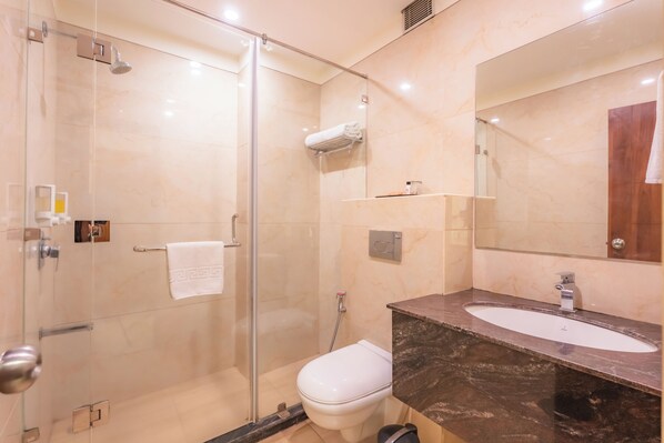 A modern bathroom with a glass shower enclosure, a white toilet, and a marble vanity with a sink. - MJ AERO SUITE (Rishikesh)