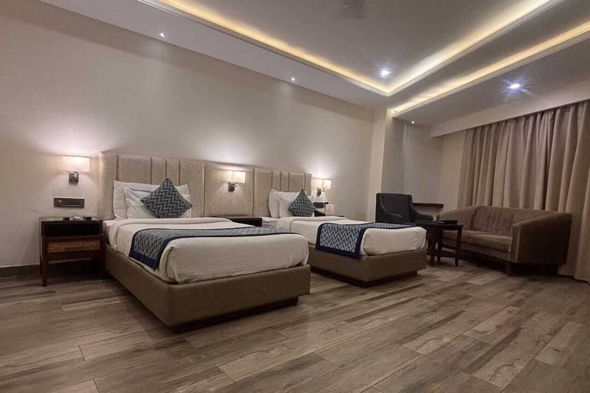 A hotel room with two beds, a sofa, a TV, and a desk.