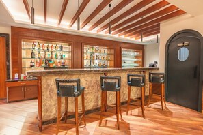A bar area with a wooden bar counter, multiple shelves of bottles, and four bar stools. - MJ AERO SUITE (Rishikesh)