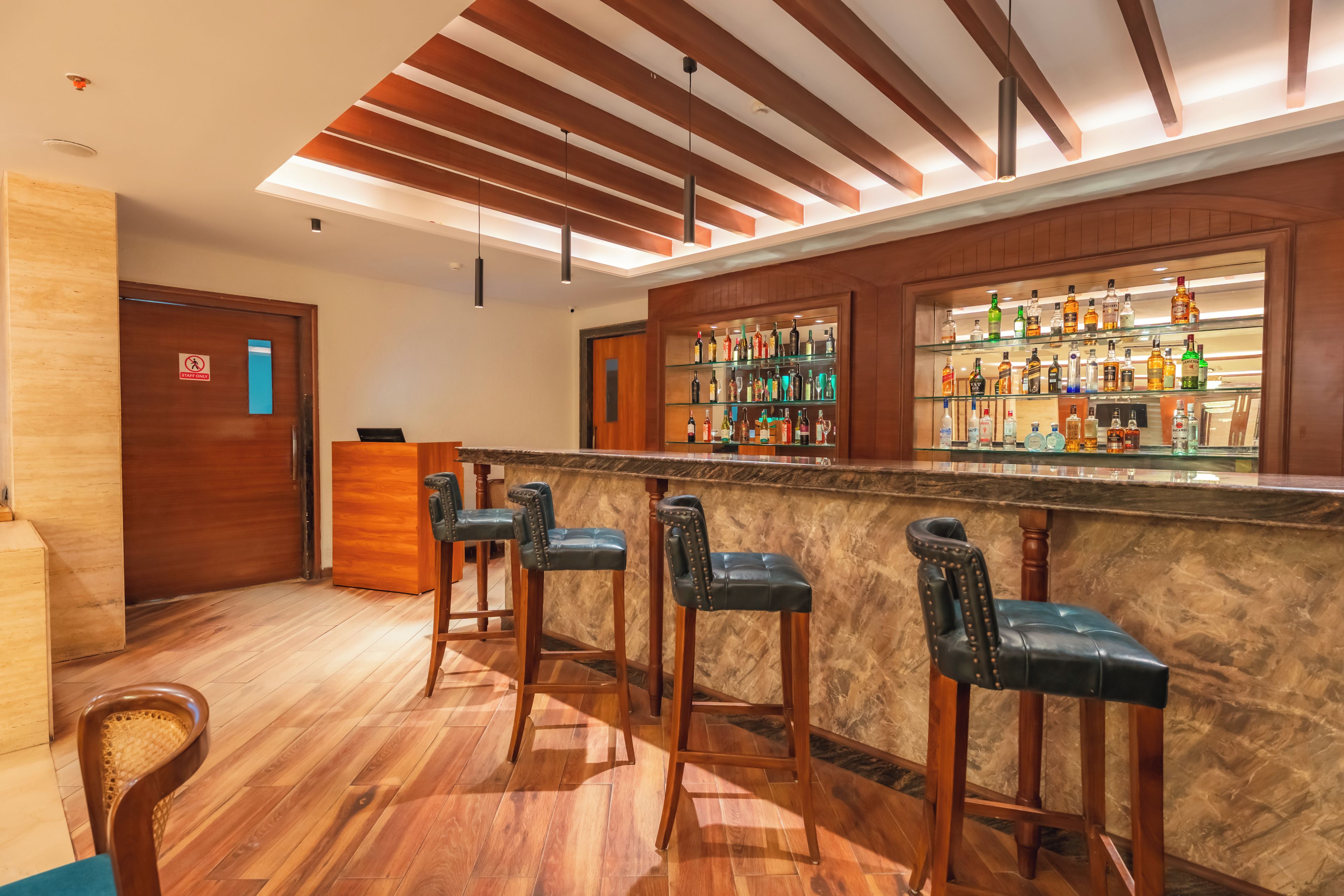 A bar area with wooden flooring, bar stools, and a shelf of liquor bottles.
