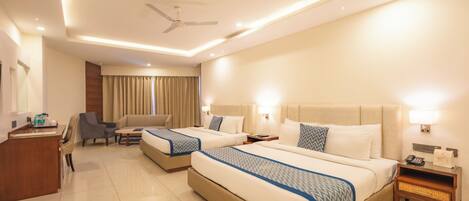 A hotel room with two beds, a desk, a chair, a ceiling fan, and a nightstand with a phone and a lamp.