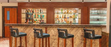 Eine Bar mit Marmorplatte, Holzstühlen und Regalen voller Flaschen und Gläsern.