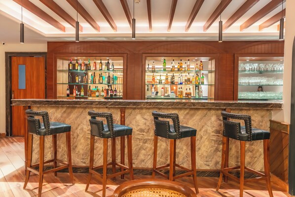 A bar area with a marble countertop, wooden stools, and shelves stocked with bottles and glasses. - MJ AERO SUITE (Rishikesh)
