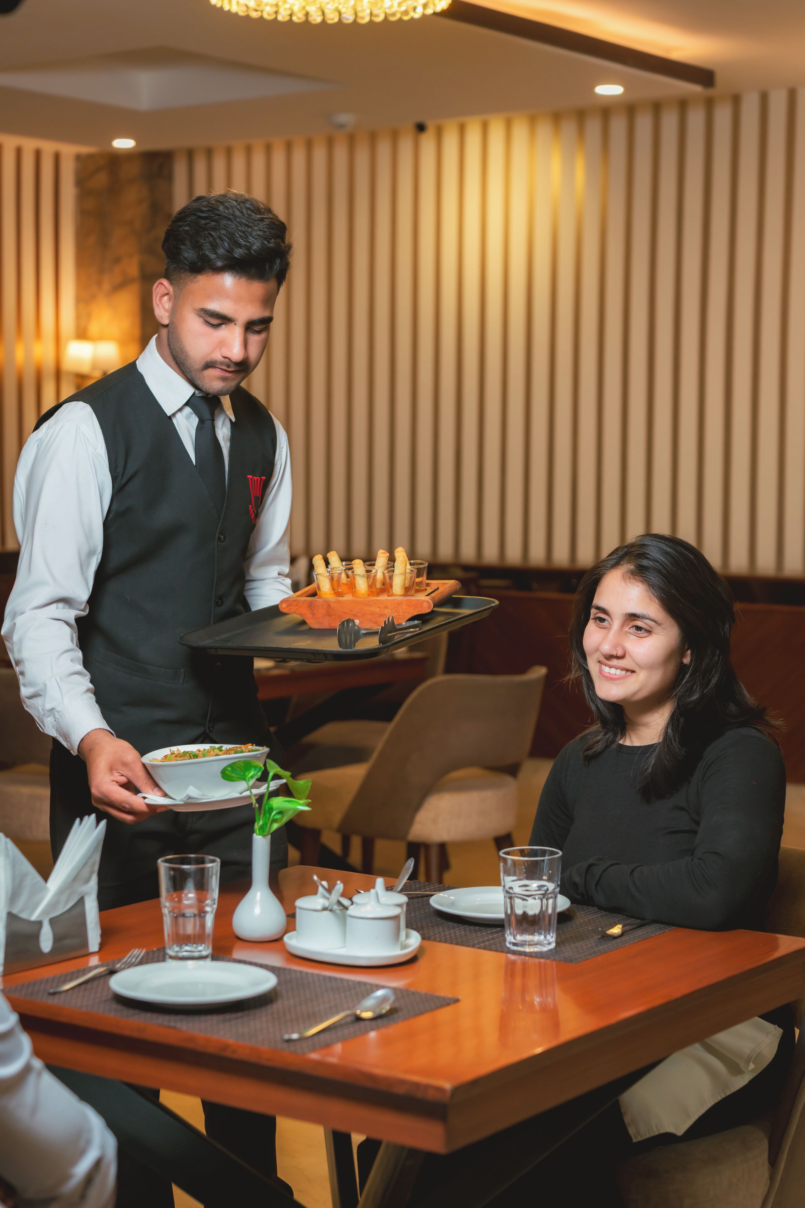 A waiter serving food to a guest at a restaurant table.