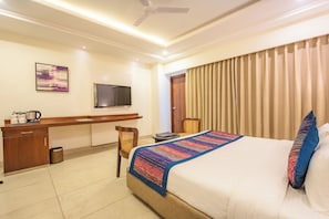 Habitación de hotel con cama, escritorio, silla, televisión y cortinas.