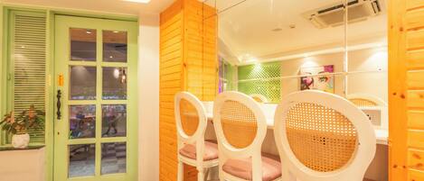 A dining area with a green door, white chairs with woven backs, and a checkered floor.