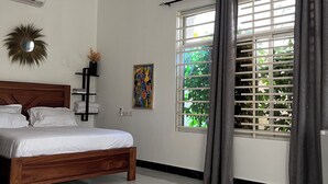 A bedroom with a wooden bed, a large window with curtains, a wall-mounted air conditioner, and a decorative mirror.