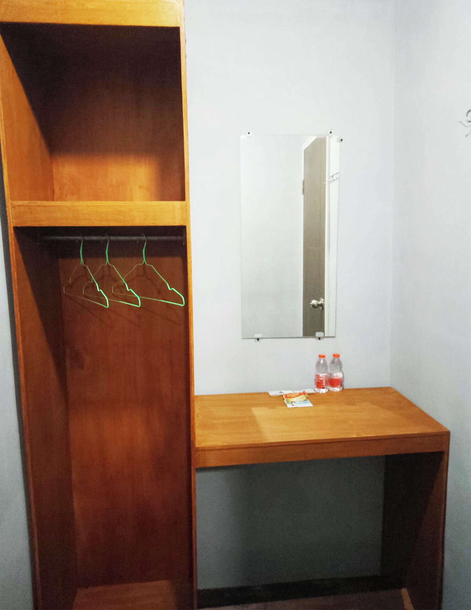 A wooden wardrobe with a mirror, a wooden desk, and a hanging rack with clothes.