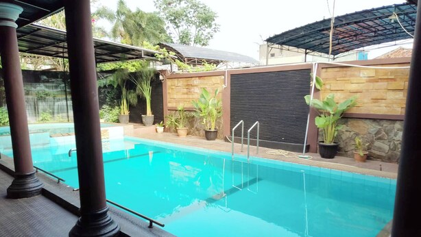 A swimming pool with clear blue water, surrounded by potted plants and a stone wall. - Guest House GS Syariah Taman Keluarga (Bekasi)