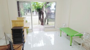 A bright room with a large glass door leading to an outdoor area, a green table, and a metal chair. - Guest House GS Syariah Taman Keluarga (Bekasi)