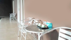 A corridor with a dining area featuring metal chairs and a table with a tray of food and a bottle. - Guest House GS Syariah Taman Keluarga (Bekasi)