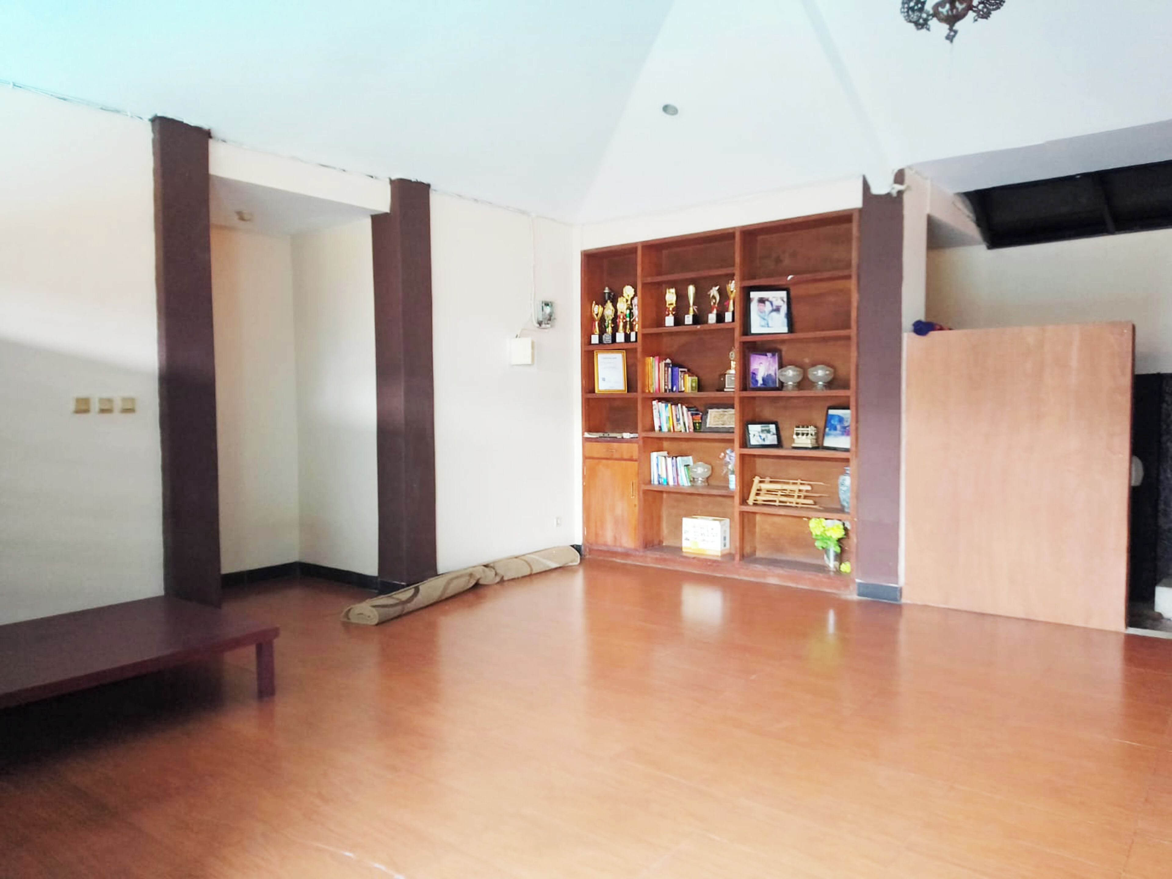 A spacious room with a wooden floor, a bench, and a bookshelf filled with trophies and books.