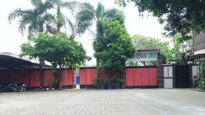 A paved courtyard with a red gate, trees, and a building with a sign reading "RENANG UMUM". - Guest House GS Syariah Taman Keluarga (Bekasi)