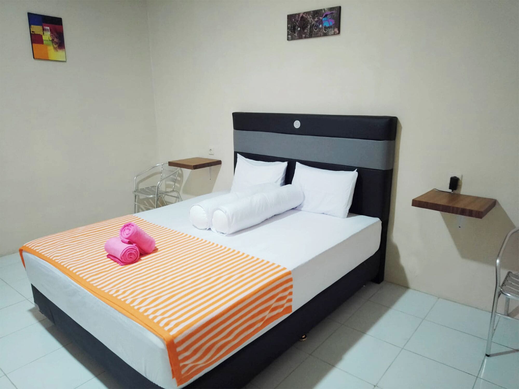 A hotel room with a bed, a chair, a small table, and a wall art piece.