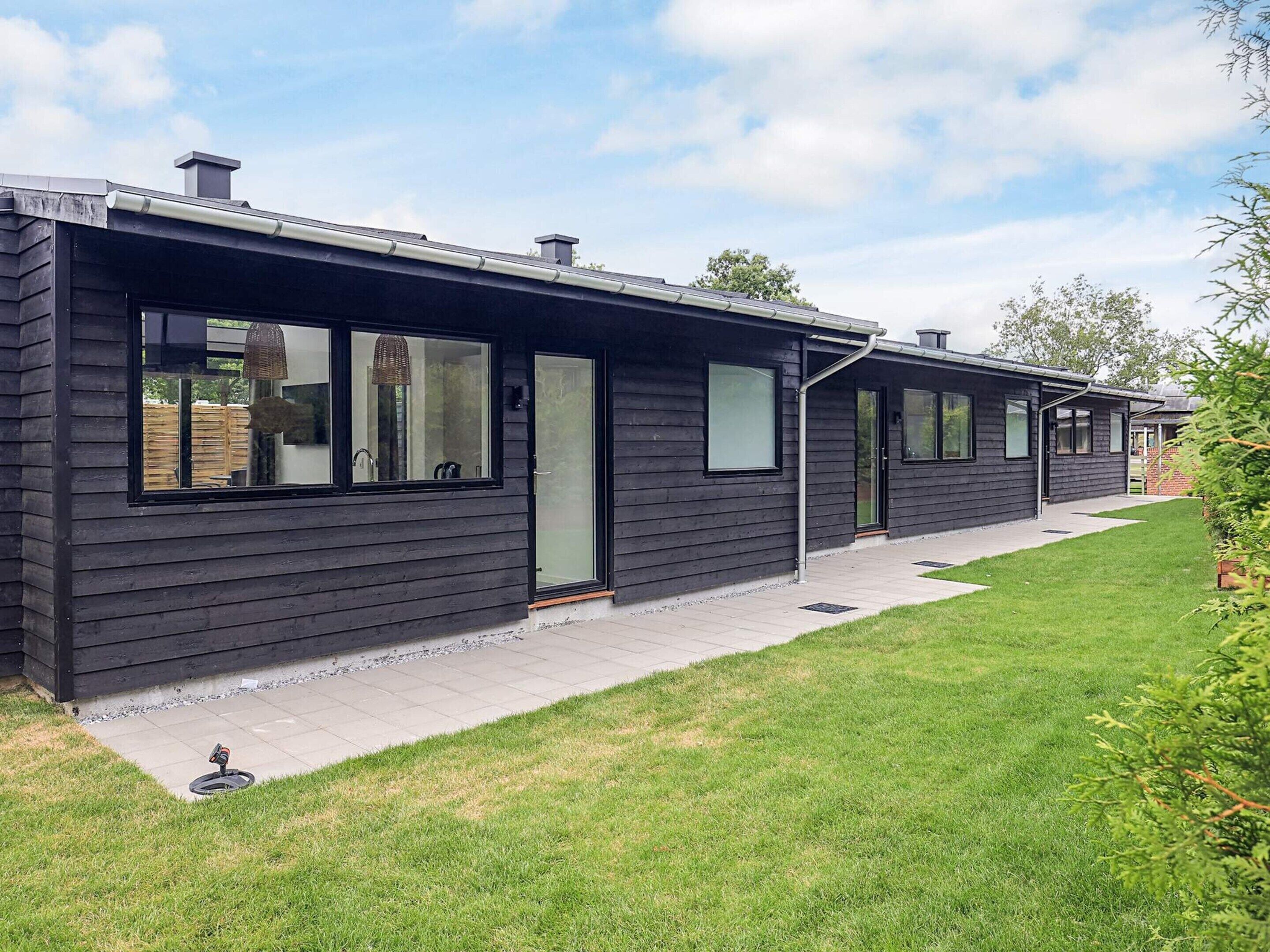 A modern two-story house with a dark exterior, large windows, and a well-maintained lawn.
