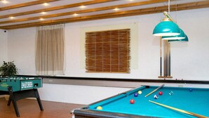 A pool table with balls and cues, a foosball table, and a hanging lamp in a room with wooden beams and a window with blinds. - 4 Person Holiday Park Home in Gilleleje (Gilleleje)