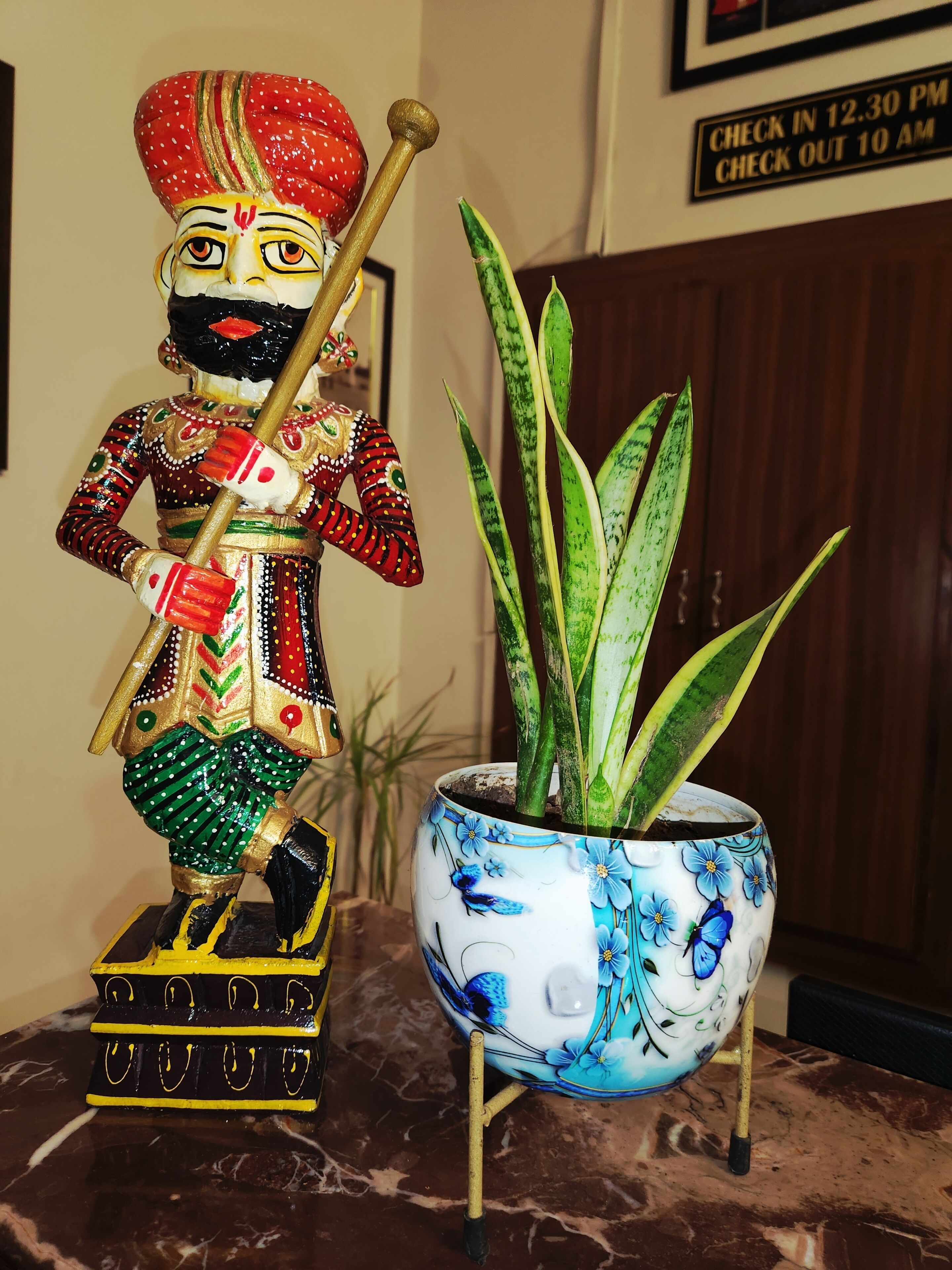 Una estàtua decorativa amb un vestit tradicional i una planta en test amb flors blaves.