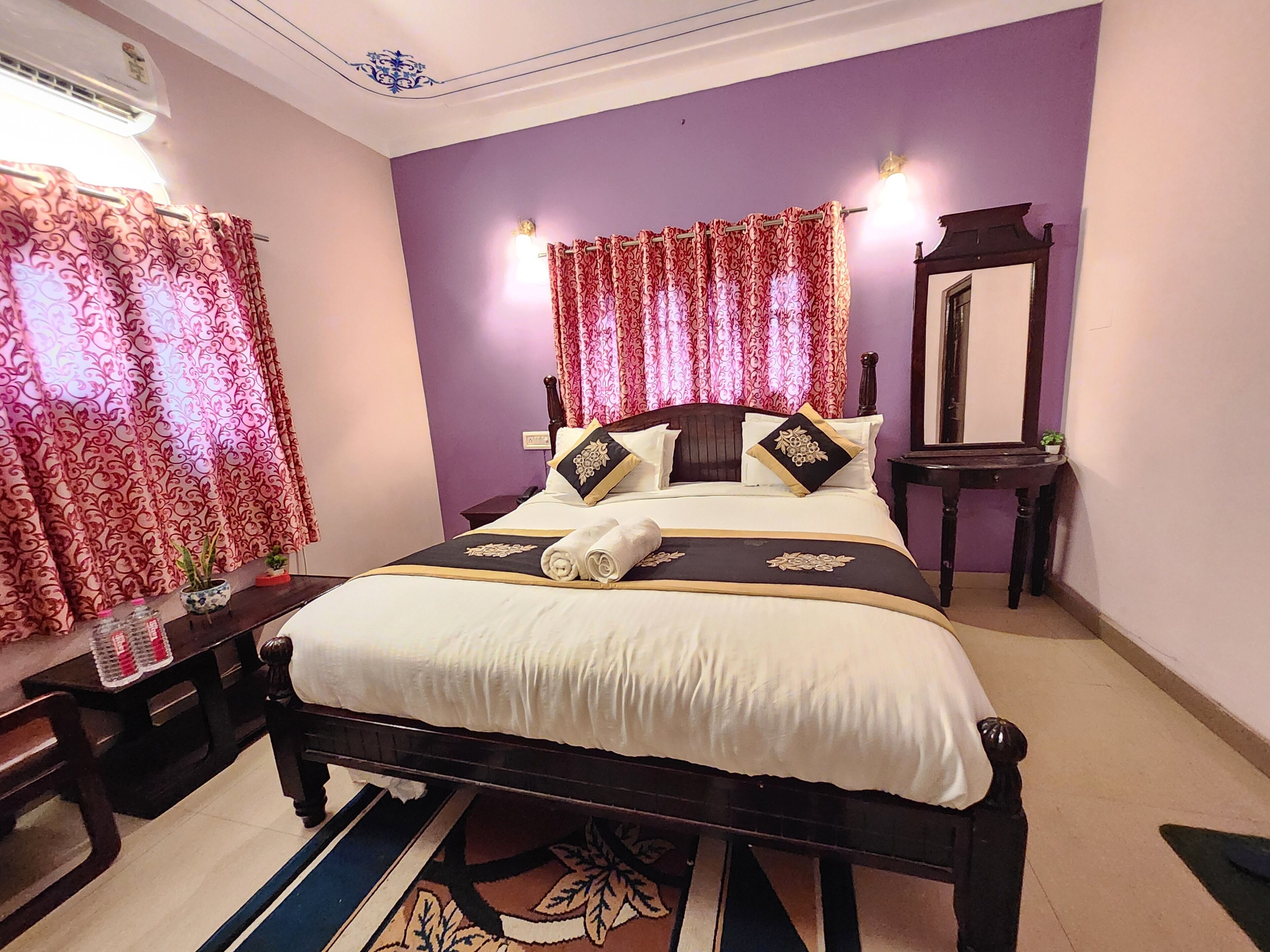 A neatly made bed with a white and black bedspread, a wooden headboard, and decorative pillows. There is a small table with a lamp beside the bed, and a mirror on the wall.