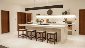 A modern kitchen with a large island, bar stools, pendant lighting, and wooden doors. - Rumah Tiha by Alfred in Bali (Canggu)