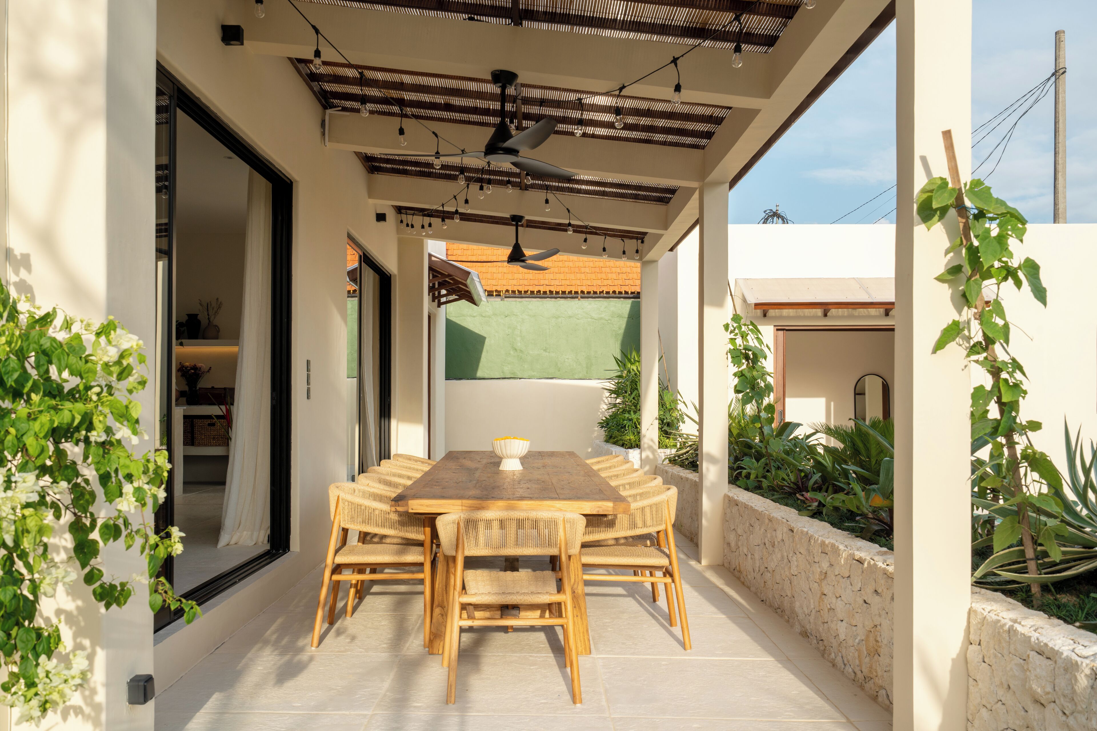 Un patio al aire libre con mesa y sillas de madera, un ventilador de techo y vistas a un campo verde.