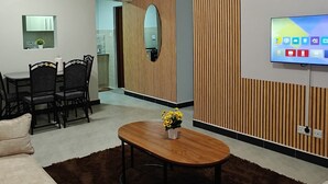 Ein modernes Wohnzimmer mit Couchtisch aus Holz, beigen Sofas und einem an der Wand montierten Fernseher.