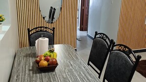Ein Essbereich mit einer Wand aus Holzlatten, einem runden Spiegel, einem Tisch mit Obstkorb und vier Stühlen.