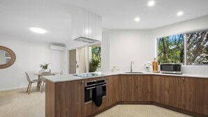 A modern kitchen with a wooden island, built-in oven, microwave, and a window with a view of trees. - Burleigh Breeze 2 Bed Beach Walk (Burleigh Heads)