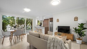 A modern living room with a sofa, TV, and dining area. - Burleigh Breeze 2 Bed Beach Walk (Burleigh Heads)