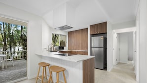 A modern kitchen with a large island, wooden cabinets, and stainless steel appliances. There are two bar stools and a view of the outdoor patio. - Burleigh Breeze 2 Bed Beach Walk (Burleigh Heads)