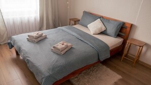 A neatly made bed with a blue blanket, two pillows, and folded towels on a wooden bed frame.