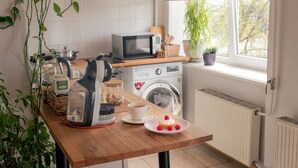 A kitchen with a microwave, washing machine, and a coffee cup on a table.