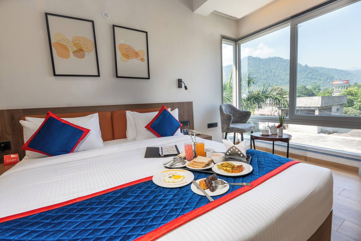 Quarto de hotel com uma cama grande, café da manhã servido na cama, uma cadeira e vista para as montanhas.