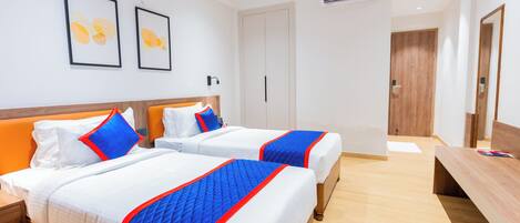 A hotel room with two beds, a wooden bench, a desk, and a wardrobe.