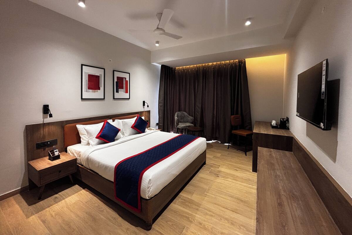 Quarto de hotel moderno com cama grande, escrivaninha, cadeira, televisão e ventoinha no teto.
