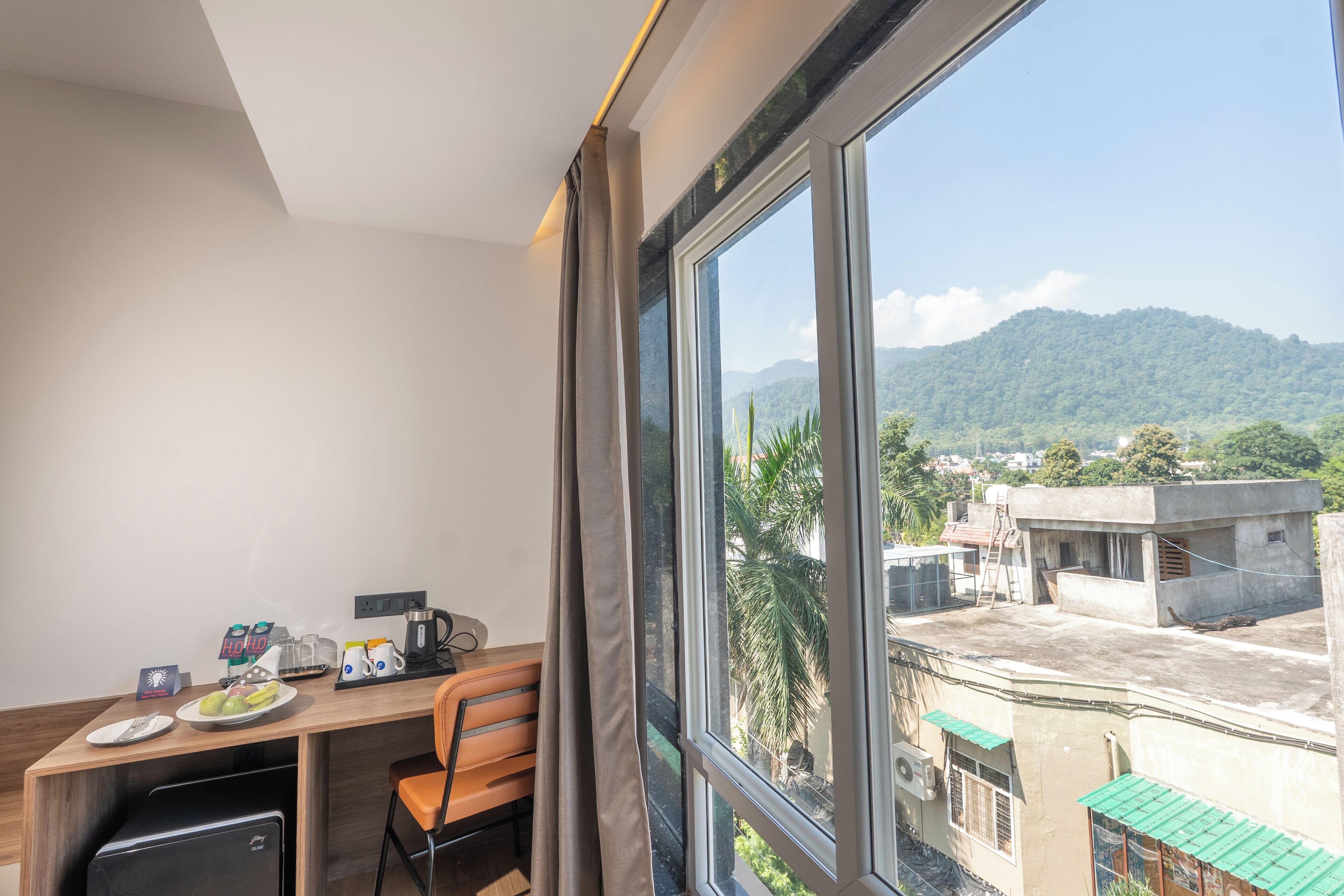 Una habitación con escritorio, silla y un amplio ventanal que ofrece vistas a una montaña y edificios.