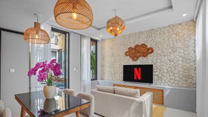 Una sala de estar moderna con una pared de piedra, un televisor de pantalla plana y una zona de comedor con mesa y sillas de vidrio.