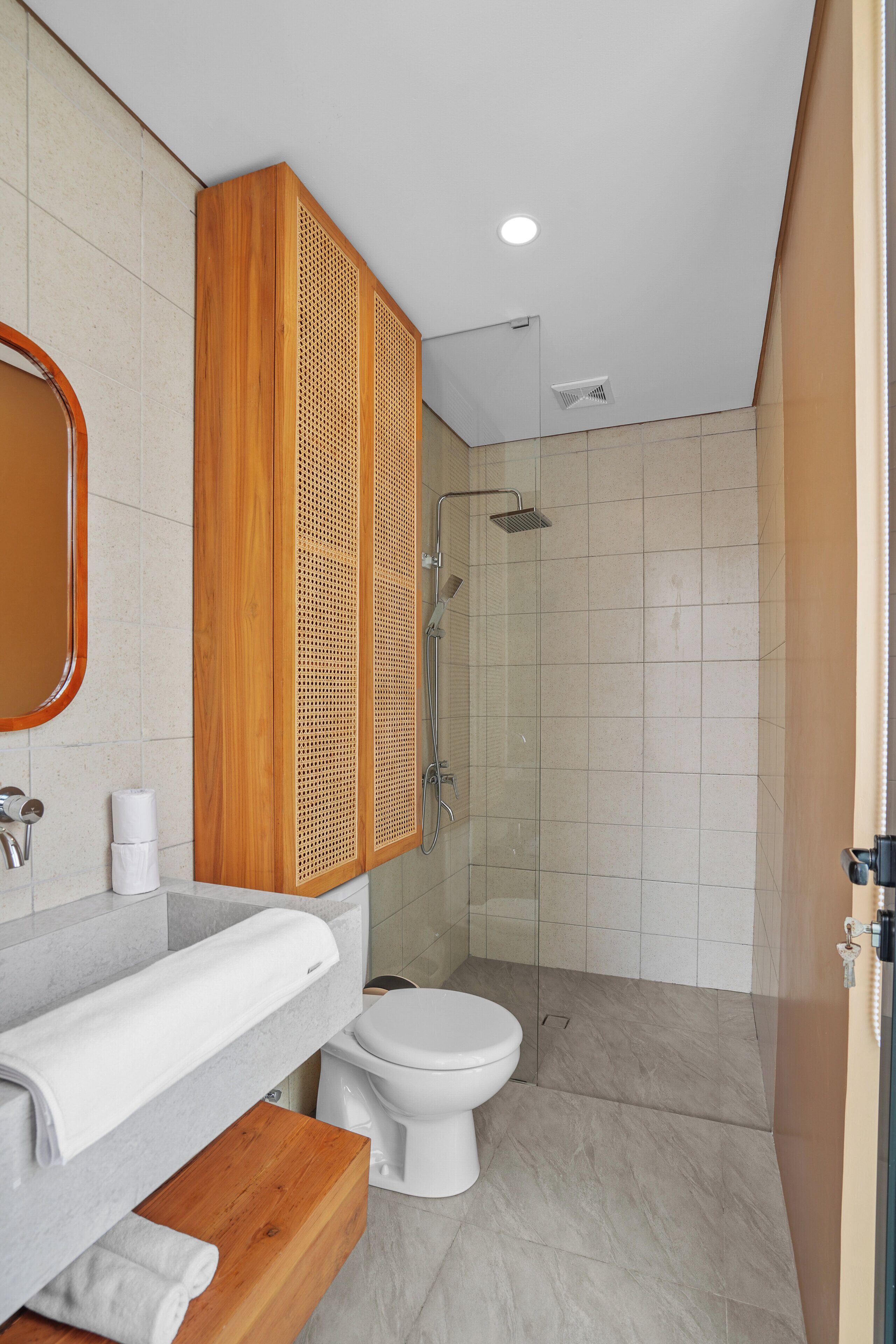 A modern bathroom with a wooden vanity, a toilet, and a glass-enclosed shower area.