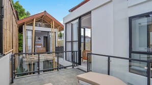 Un edificio moderno con balcón de vidrio, terraza de madera y un espacio exterior cubierto.