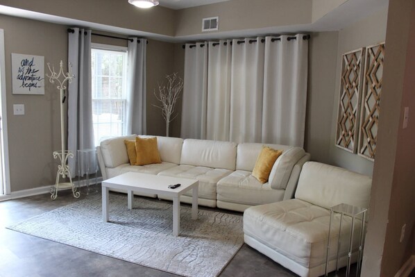 A living room with a white sectional sofa, a coffee table, and a patterned rug.