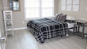 A bedroom with a bed, a nightstand, a mirror, and a window with blinds.
