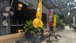 An outdoor seating area with tables and chairs, a hanging fan, and potted plants.