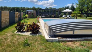 A backyard with a swimming pool, a covered patio, and a fenced area with outdoor furniture.
