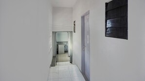 A narrow hallway with white walls and a tiled floor leading to a kitchen area.